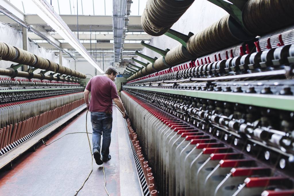 Male factory worker monitoring weaving machines in woollen mill