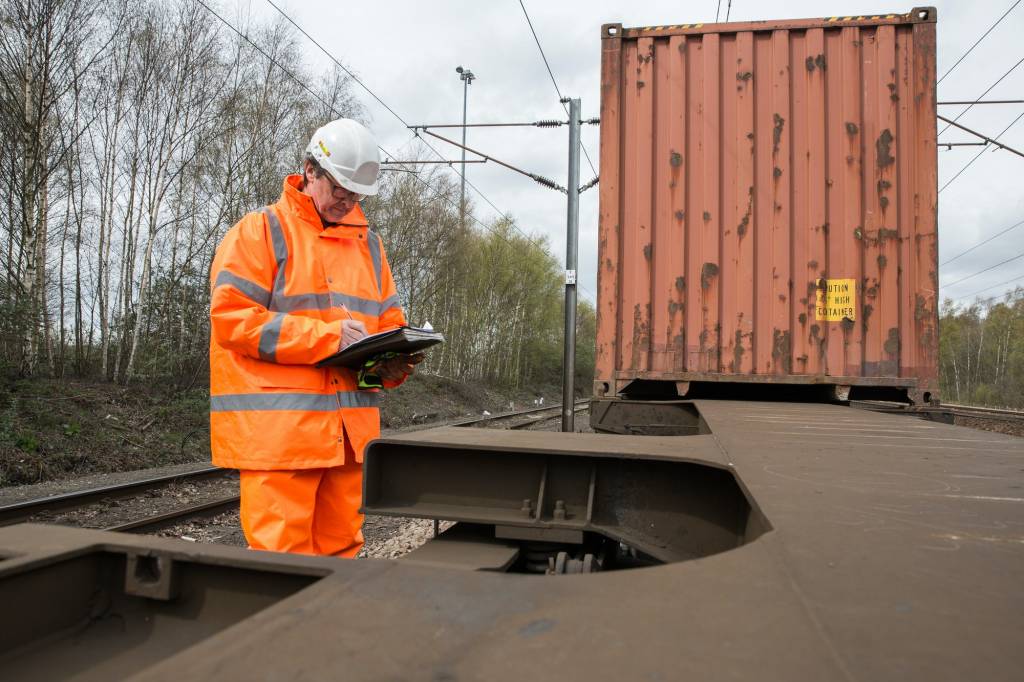 railroad engineer inspecting and maintaining shipping container freight wagons in the rail industry